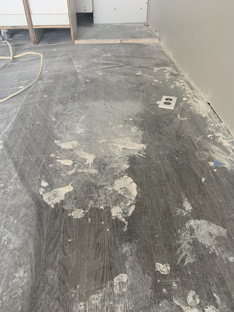 Apartment floor covered in construction debris and drywall compound before cleaning